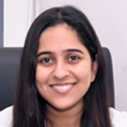 Smiling portrait of a woman with long black hair, dressed in formal attire, sitting in an office chair.