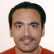 A middle-aged man with short hair and a light beard, wearing an orange shirt, smiling and looking at the camera.