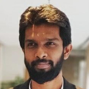 A man with a beard and short hair, wearing a dark shirt, smiling slightly while looking directly at the camera.