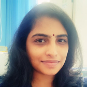Portrait of a woman with black hair and a bindi, smiling softly in a casual setting.