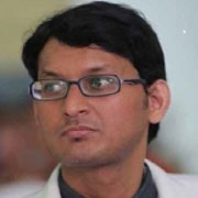 A man with glasses and short hair, dressed in a white shirt, looking thoughtfully to the side.