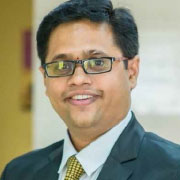 A man in a business suit with glasses smiling confidently.