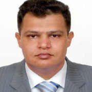 A professional portrait of a man wearing a grey suit and a light blue tie, with short hair and a serious expression.