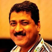 : A close-up portrait of a smiling man with a mustache, wearing a striped shirt with a badge around his neck.