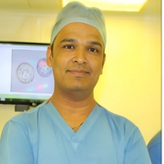 A man wearing surgical scrubs and a cap, standing in front of a screen displaying images of embryos in a laboratory setting.