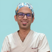 A smiling doctor in scrubs and glasses wearing a medical cap.